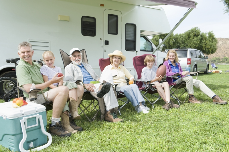 smiling family with children, parents and grandparents siting on folding chairs outside a camper in an RV park